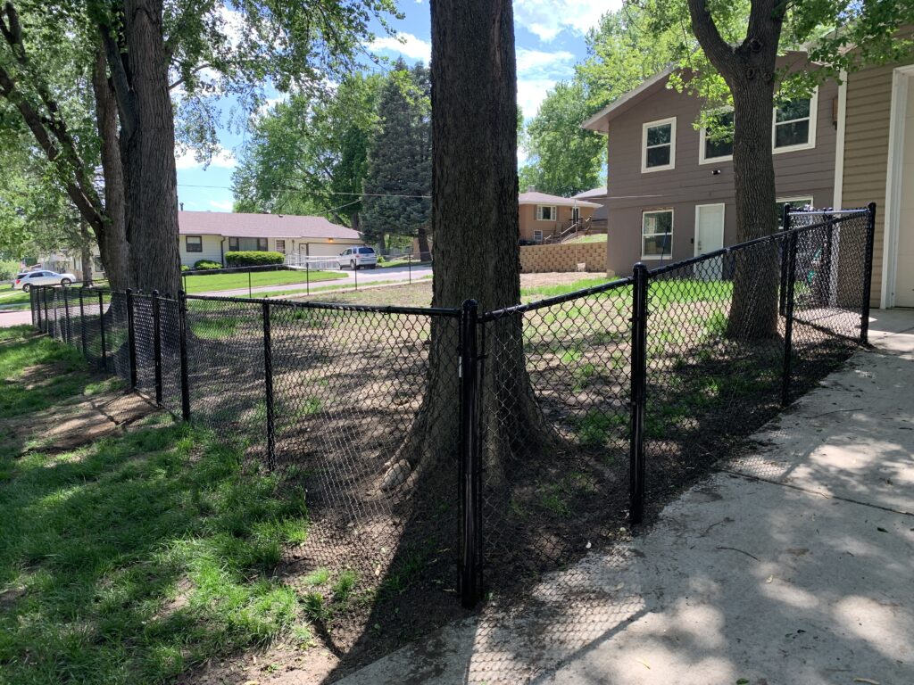 Modern black vinyl-coated chain link fence installation providing sleek security for a residential backyard in Hartford, SD.